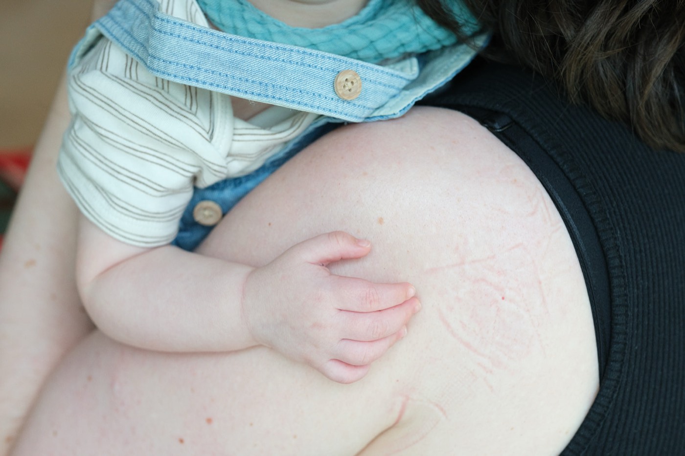 A baby's hand resting on their mum's shoulder at the pilot